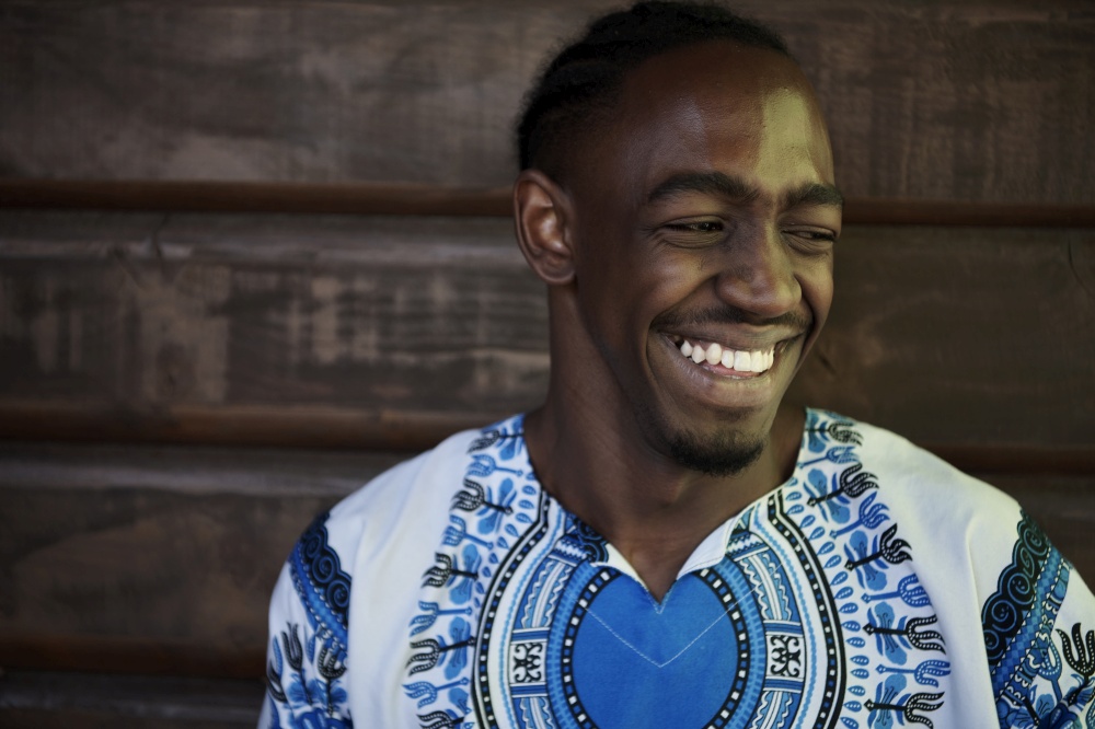 Close up portrait of a smiling young african man wearing traditioinal clothes standing isolated over yellow wall background