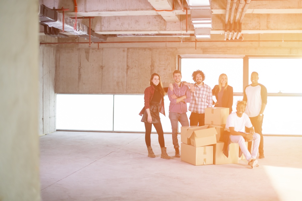 portrait of happy multiethnic business team with sunlight through the windows and cardboard boxes around them during movin in at new unfinished startup office building