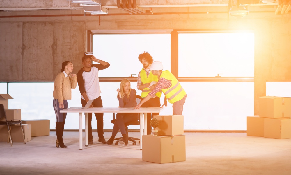 young multiethnic business team checking documents and business workflow on construction site using the virtual reality headset and laptop computer with sunlight through the windows during moving in at new startup office