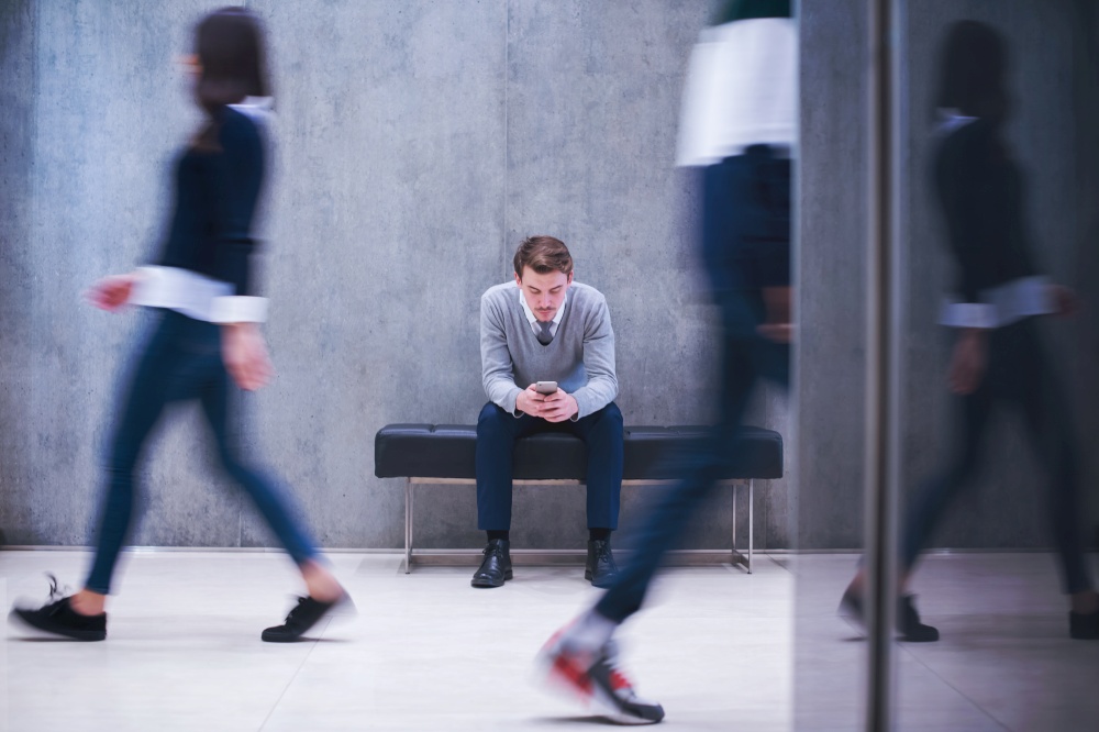 young businessman using smart phone while sitting on the bench at busy office lobby during a break