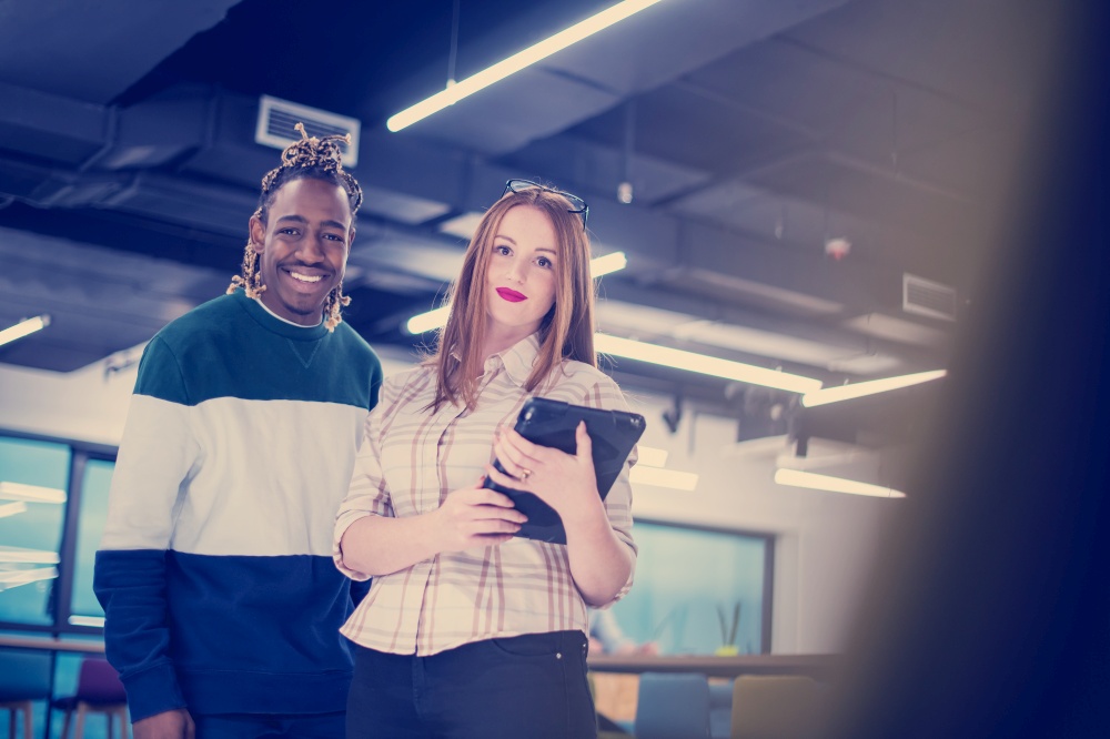 young multiethnic business couple african american guy and his redhead female colleague using a tablet computer while standing in modern startup office