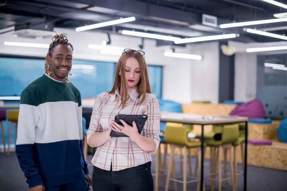 young multiethnic business couple african american guy and his redhead female colleague using a tablet computer while standing in modern startup office