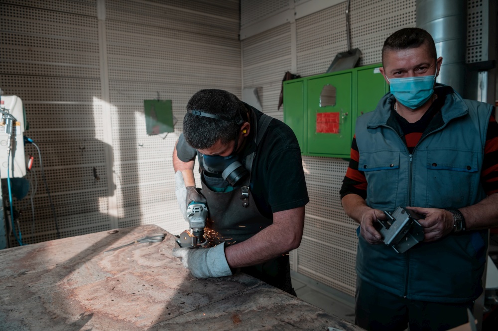 Industrial work during a pandemic. Two men work in a heavy metal factory, wearing a mask on their faces due to a coronavirus pandemic. High quality photo. Industrial work during a pandemic. Two men work in a heavy metal factory, wearing a mask on their face due to a coronavirus pandemic