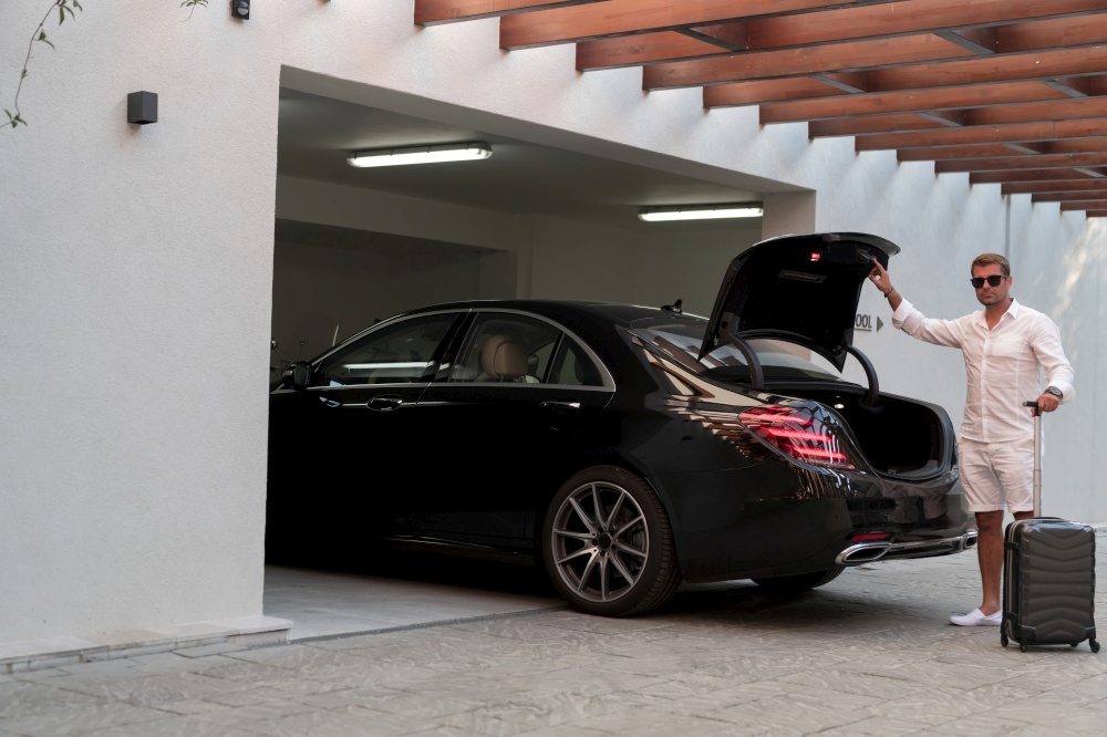 A senior man in a garage with glasses and modern casual clothes takes out his suitcases from the car. Selective focus. High-quality photo. A senior man in a garage with glasses and modern casual clothes takes out his suitcases from the car. Selective focus