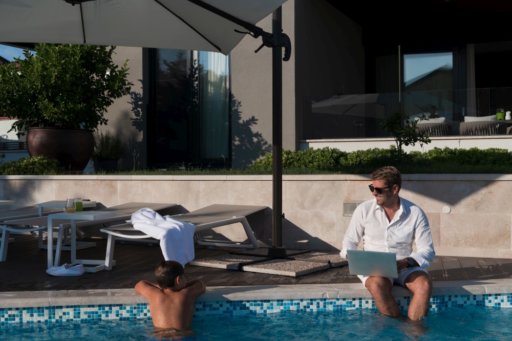 A modern elderly man enjoys the pool while working on his laptop next to a modern luxury house. Selective focus. High-quality photo. A modern elderly man enjoys the pool while working on his laptop next to a modern luxury house. Selective focus