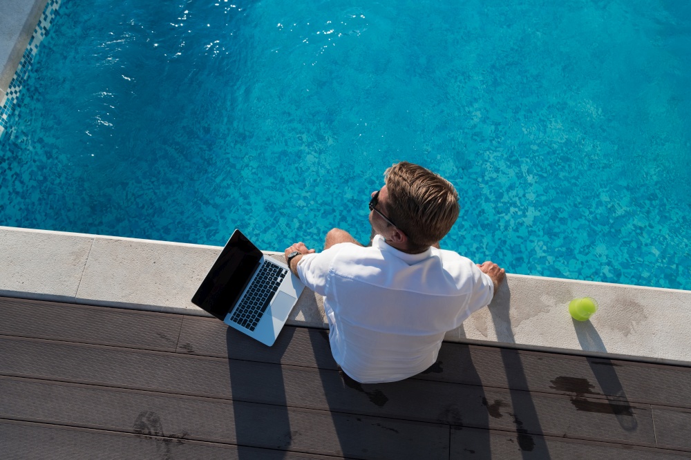 A modern elderly man enjoys the pool while working on his laptop next to a modern luxury house. Selective focus. High-quality photo. A modern elderly man enjoys the pool while working on his laptop next to a modern luxury house. Selective focus