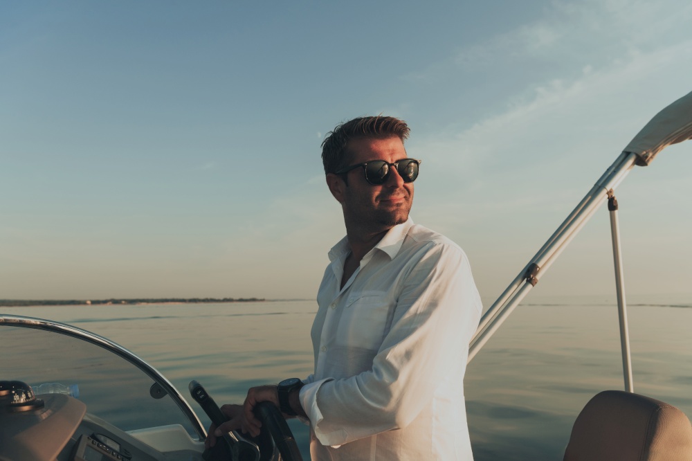 A determined senior businessman in casual clothes and sunglasses enjoys his vacation driving a luxury boat at sunset. Selective focus. High-quality photo. A determined senior businessman in casual clothes and sunglasses enjoys his vacation driving a luxury boat at sunset. Selective focus