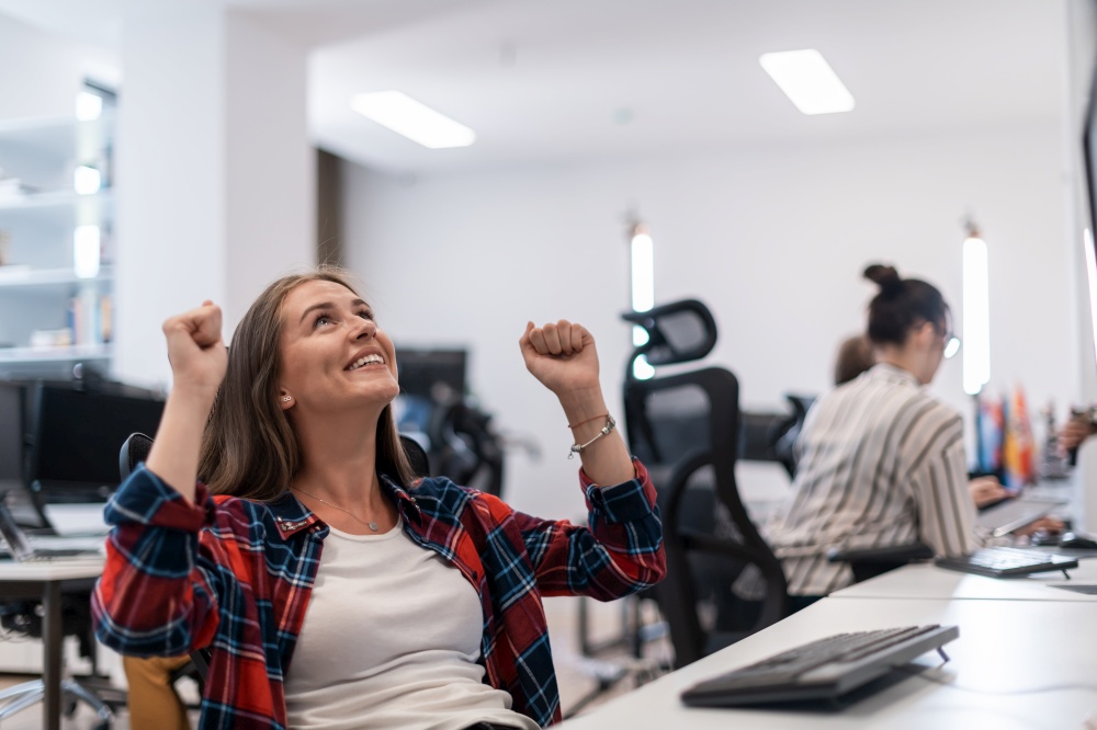 Happy casual businesswoman celebrating success while working on a desktop computer in a modern open plan startup office interior. Selective focus. High-quality photo. Happy casual business woman celebrating success while working on desktop computer in modern open plan startup office interior. Selective focus