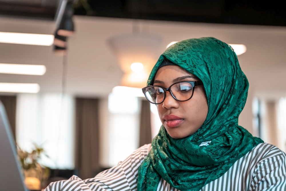 Businesswoman wearing a green hijab using laptop in relaxation area at modern open plan startup office. Selective focus. High-quality photo. Business woman wearing a green hijab using laptop in relaxation area at modern open plan startup office. Selective focus