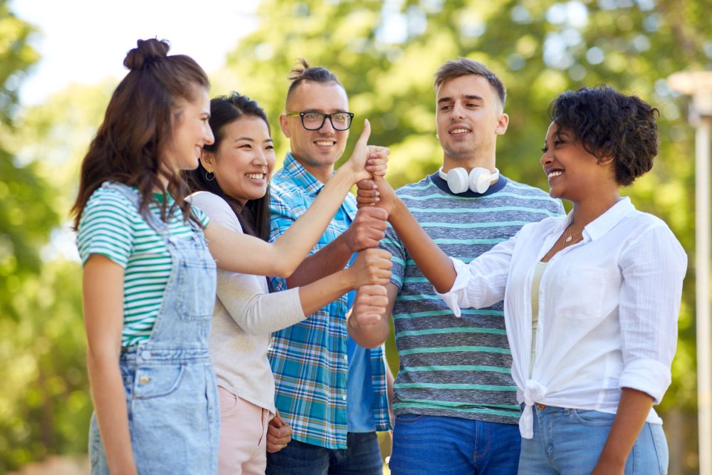 success, friendship and international concept - group of happy smiling friends making thumbs up gesture in park. happy friends making thumbs up gesture in park