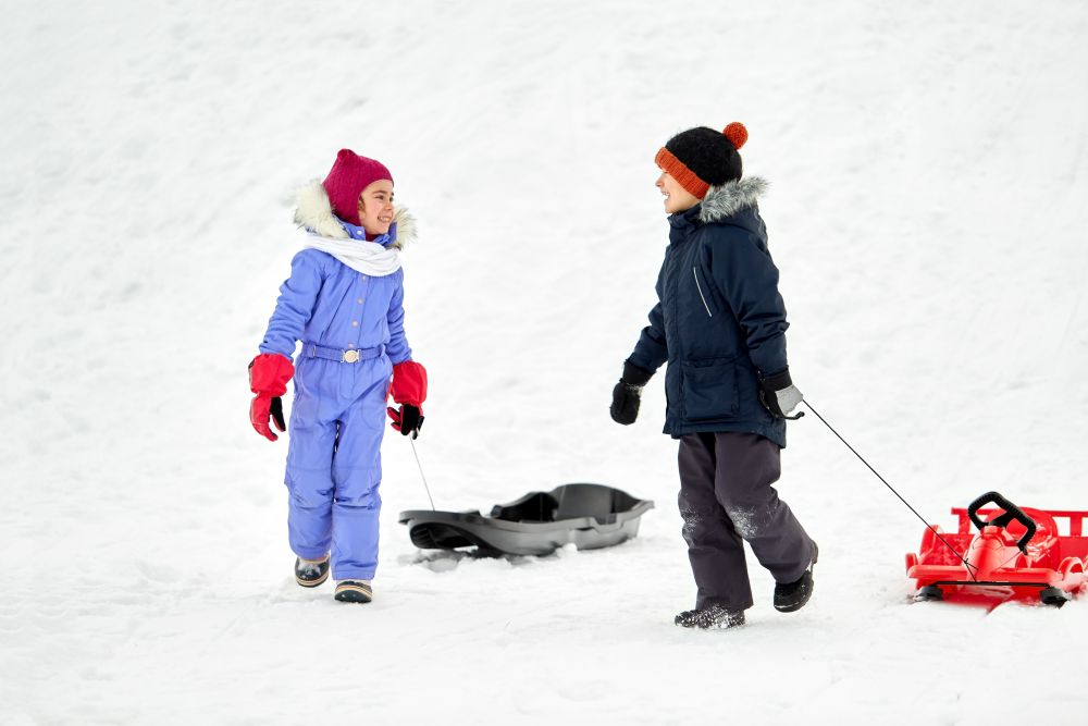 childhood, sledging and season concept - happy little kids with sleds in winter. happy little kids with sleds in winter