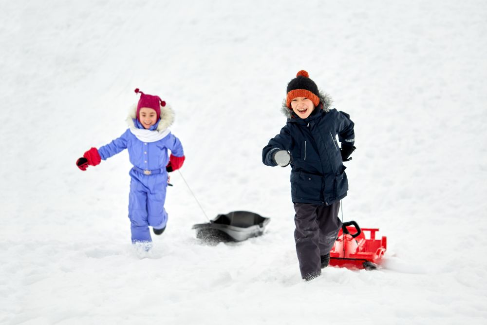 childhood, leisure and season concept - happy little kids in winter clothes with sled having fun outdoors. happy kids with sled having fun outdoors in winter