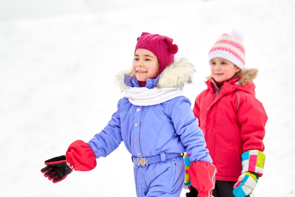 childhood, leisure and season concept - happy little girls in in winter clothes outdoors. happy little girls in winter clothes outdoors