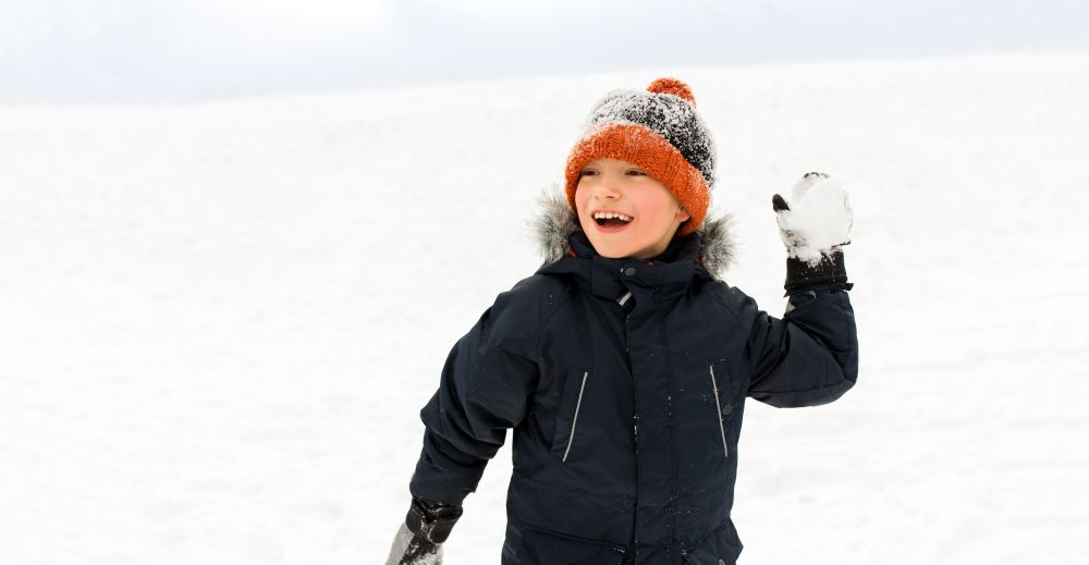 childhood, leisure and season concept - happy little boy throwing snowball in winter. happy boy playing and throwing snowball in winter