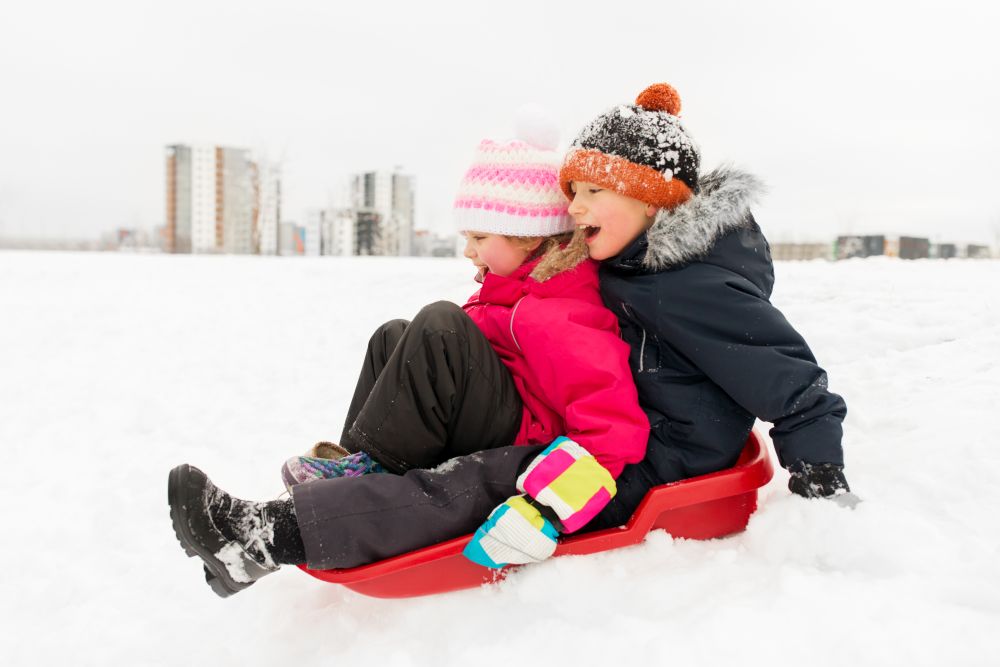 childhood, sledging and season concept - happy little kids sliding on sled down snow hill in winter. little kids sliding on sled down hill in winter