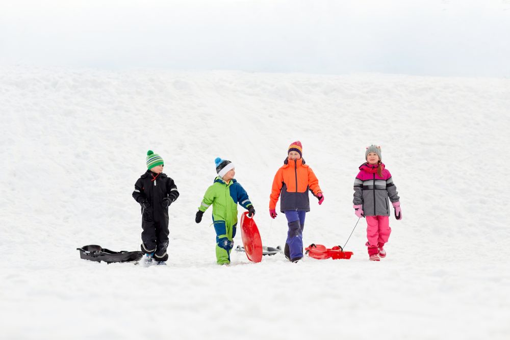 childhood, sledging and season concept - group of happy little kids with sleds outdoors in winter. happy little kids with sleds sledging in winter