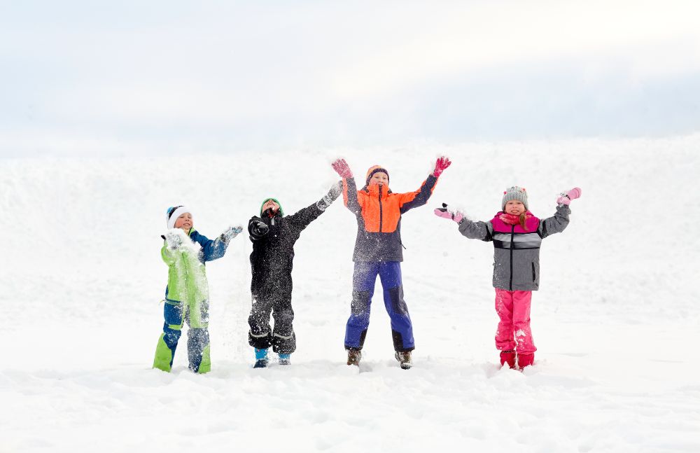 childhood, leisure and season concept - group of happy little kids in winter clothes playing with snow outdoors. happy little kids playing outdoors in winter