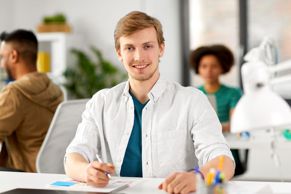 business and people concept - smiling creative man sitting at office table. smiling creative man sitting at office table