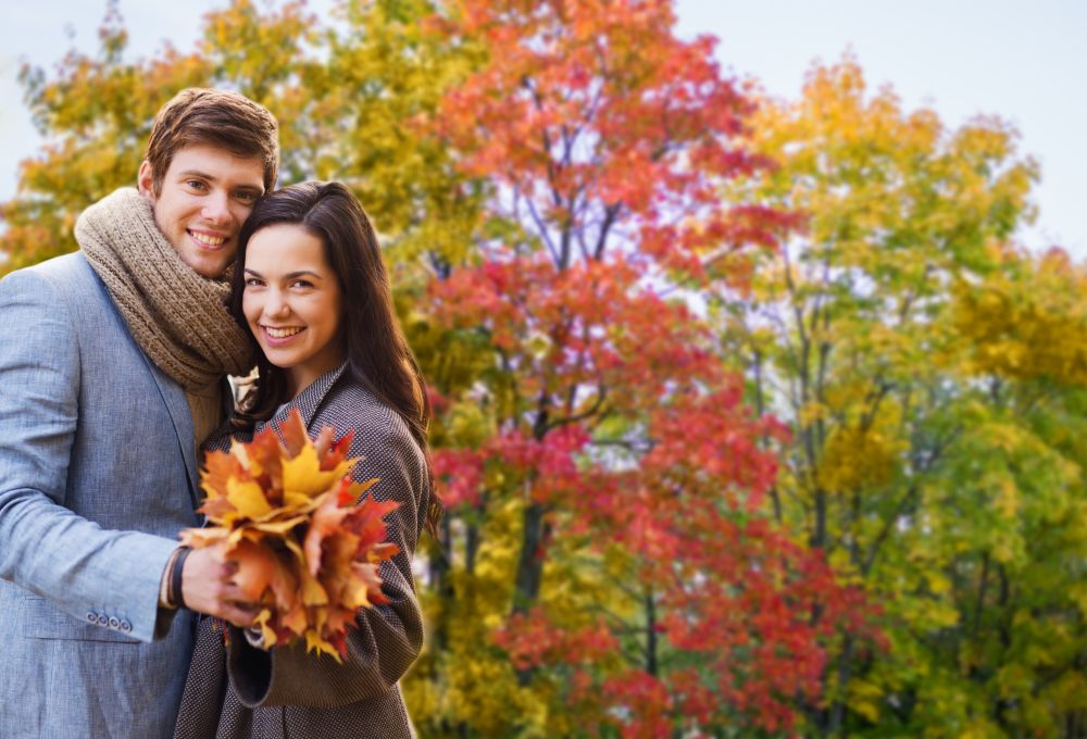 love, relationship and season concept - smiling couple with bunch of maple leaves hugging over autumn park background. smiling couple hugging in autumn park