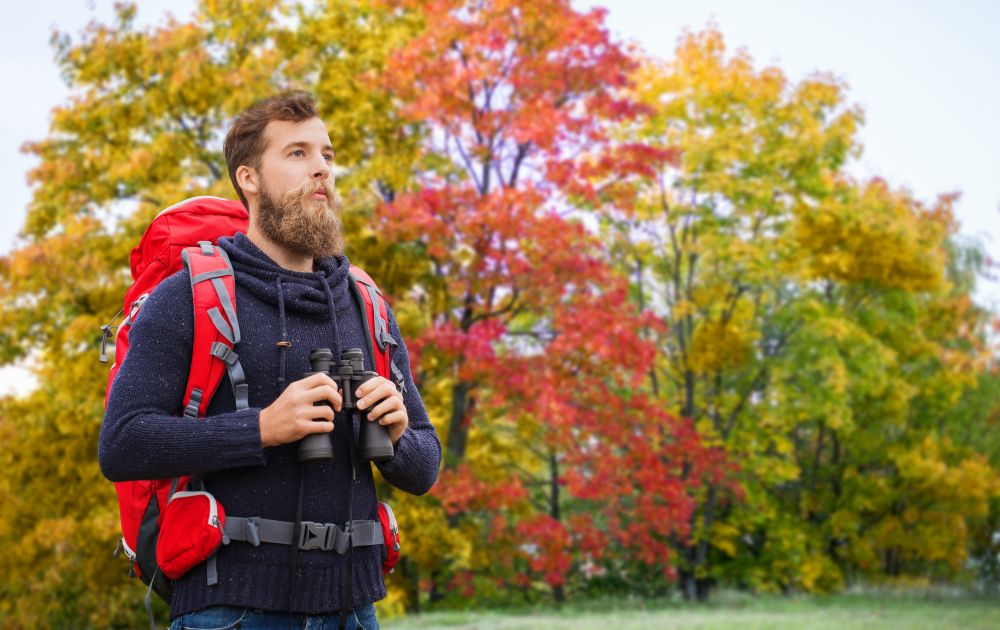adventure, travel, tourism, hike and people concept - man with red backpack and binocular outdoors. man with backpack and binocular outdoors