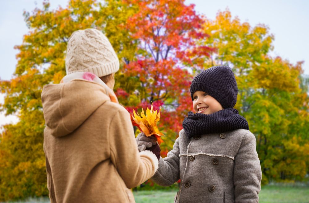 childhood, season and love concept - smiling little boy giving maple leaves to girl over autumn park background. kids with autumn maple leaves over park background