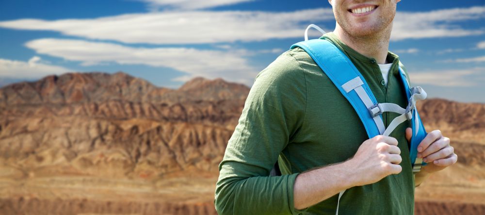 adventure, travel, tourism, hike and people concept - close up of smiling man with backpack over grand canyon national park background. close up of man with backpack over grand canyon