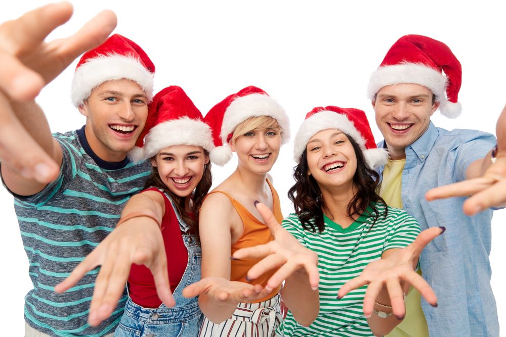 christmas, holidays and friendship concept - group of happy smiling friends in santa hats having fun over white background. happy friends in santa hats over white background