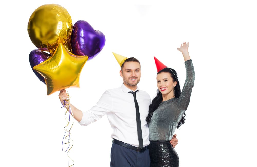 people, celebration and holidays concept - happy couple with party caps and balloons. happy couple with party caps and balloons