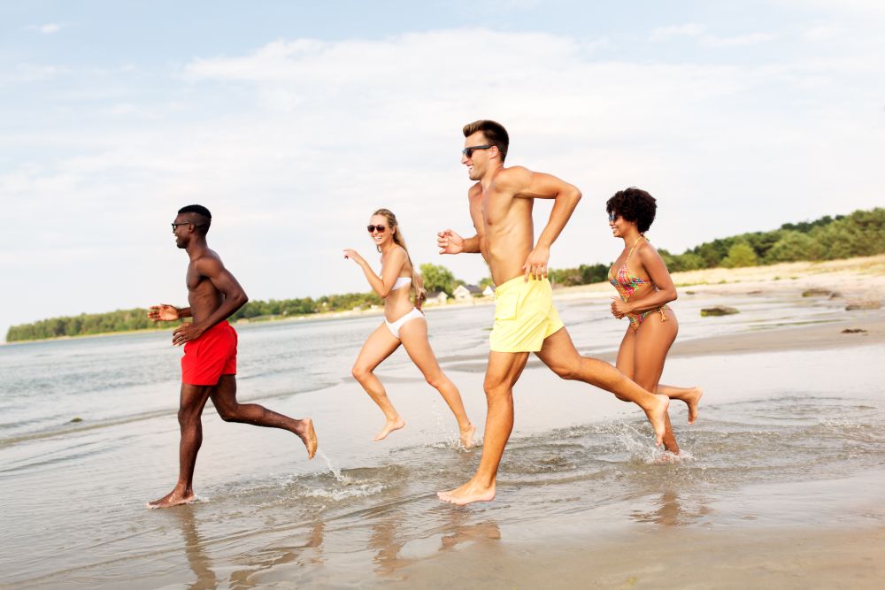 friendship, summer holidays and people concept - happy friends running on beach. happy friends running on summer beach