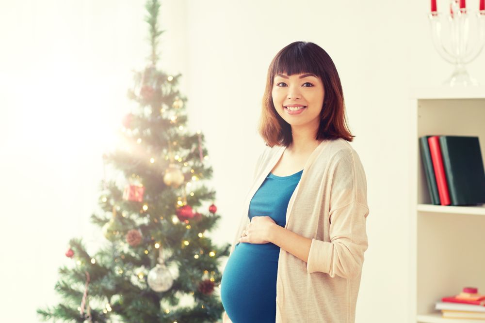 pregnancy, winter holidays and people concept - happy asian pregnant woman at christmas tree at home. happy pregnant woman at christmas tree at home