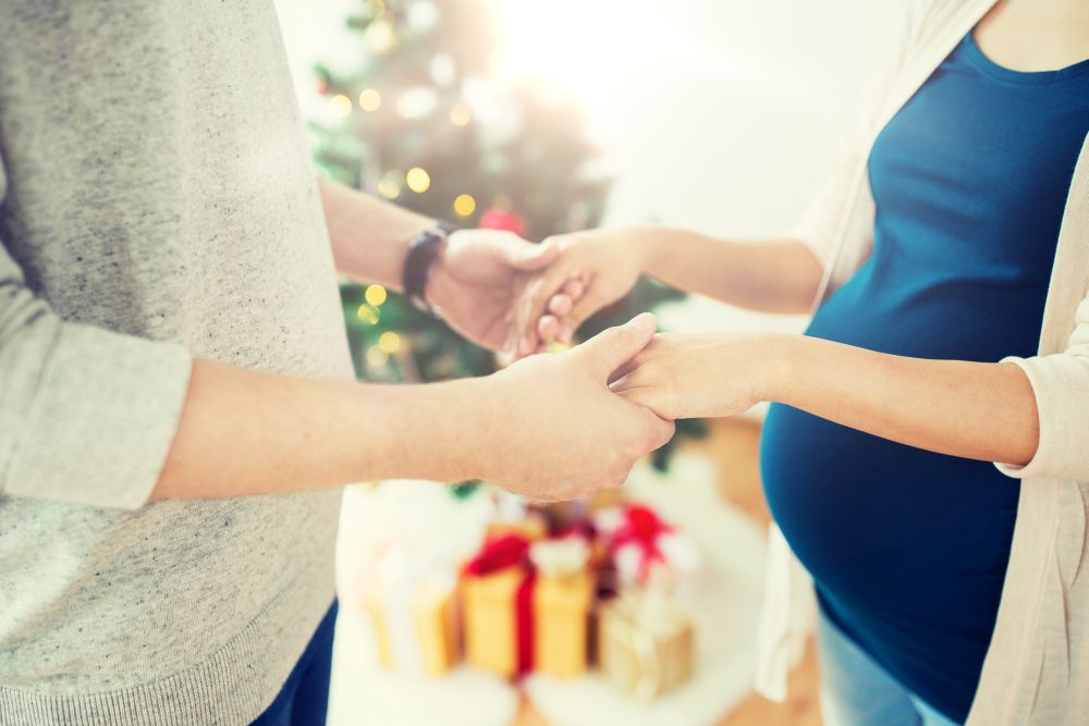 pregnancy, winter holidays and people concept - close up of happy couple holding hands at christmas. close up of man and pregnant woman at christmas