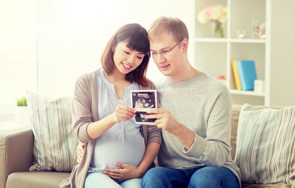 pregnancy, family and people concept - happy husband with his pregnant wife looking at baby ultrasound images at home. happy couple with ultrasound images at home
