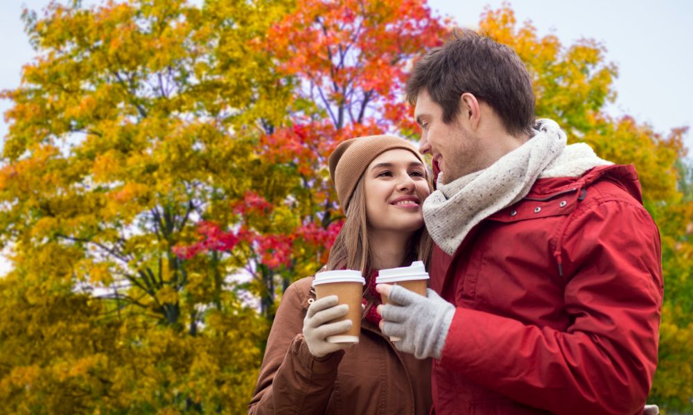 love, relationships, season and people concept - happy young couple with takeaway coffee over autumn park background. happy couple with coffee walking in autumn park