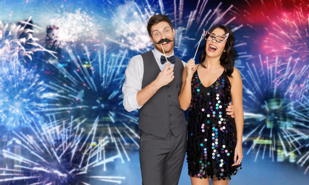 celebration, fun and holidays concept - happy couple posing with party props over firework background. happy couple with party props having fun