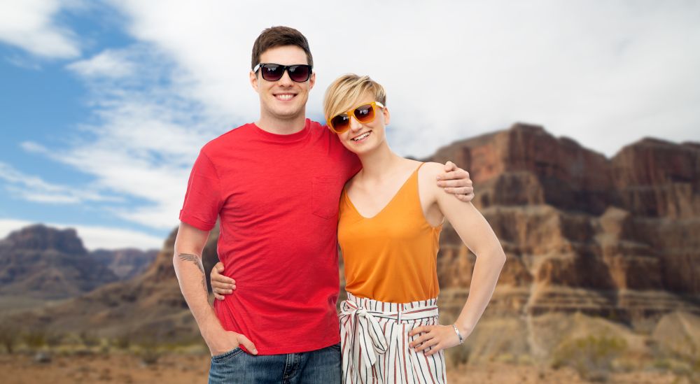 summer fashion, style and people concept - smiling couple in sunglasses hugging over grand canyon national park background. couple in sunglasses hugging