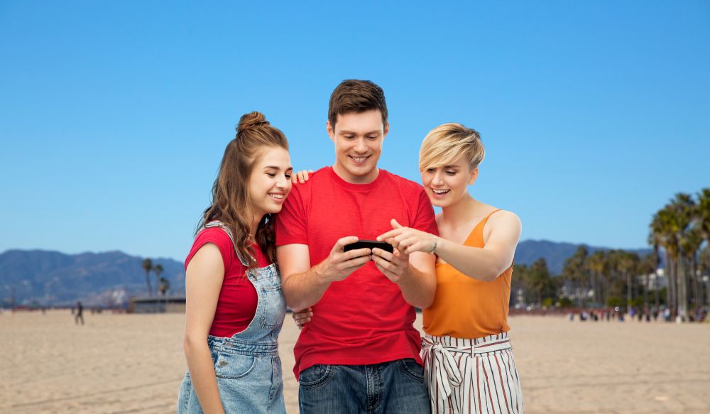 travel, tourism and summer holidays concept - group of happy smiling friends with smartphone over venice beach background in california. friends with smartphone