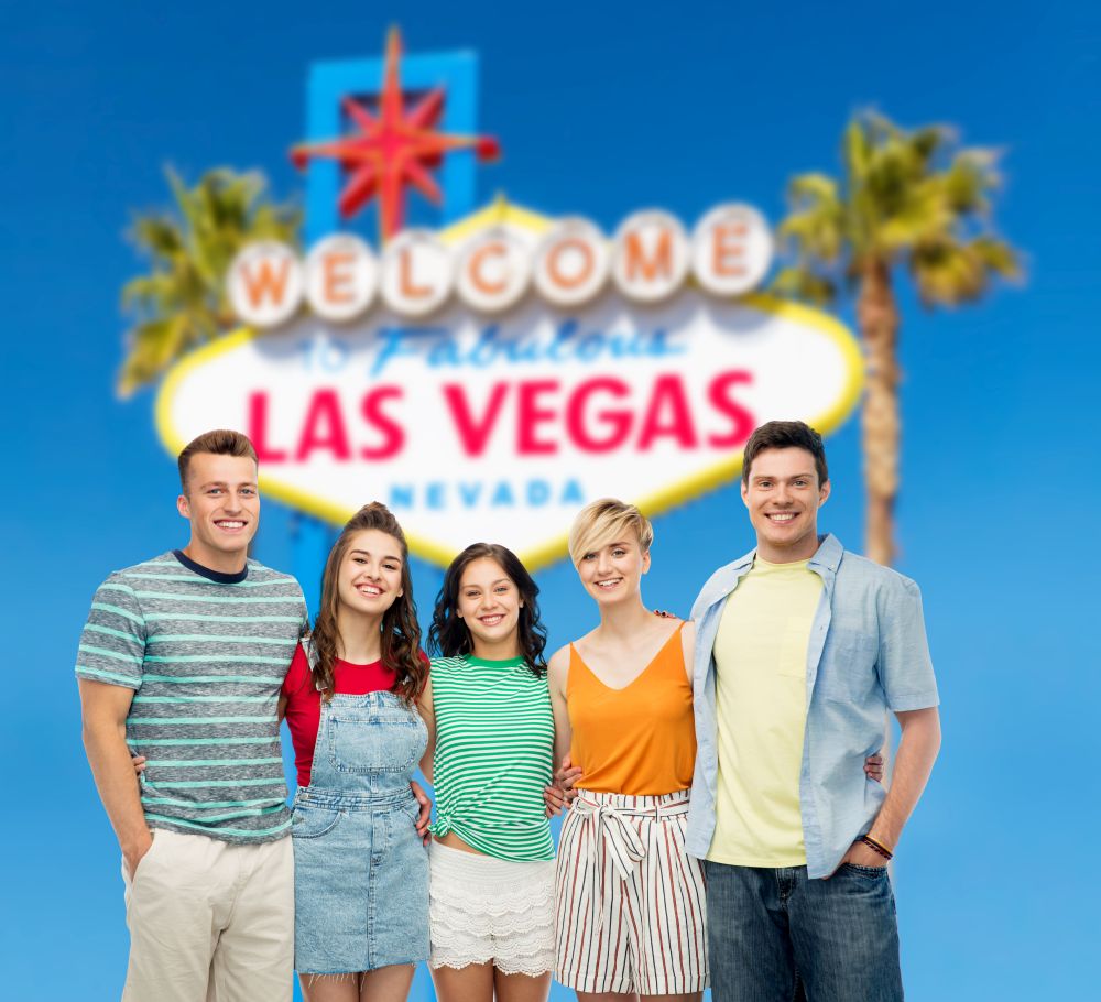 entertainment, leisure and friendship concept - group of happy smiling friends hugging over welcome to fabulous las vegas sign background. happy friends hugging