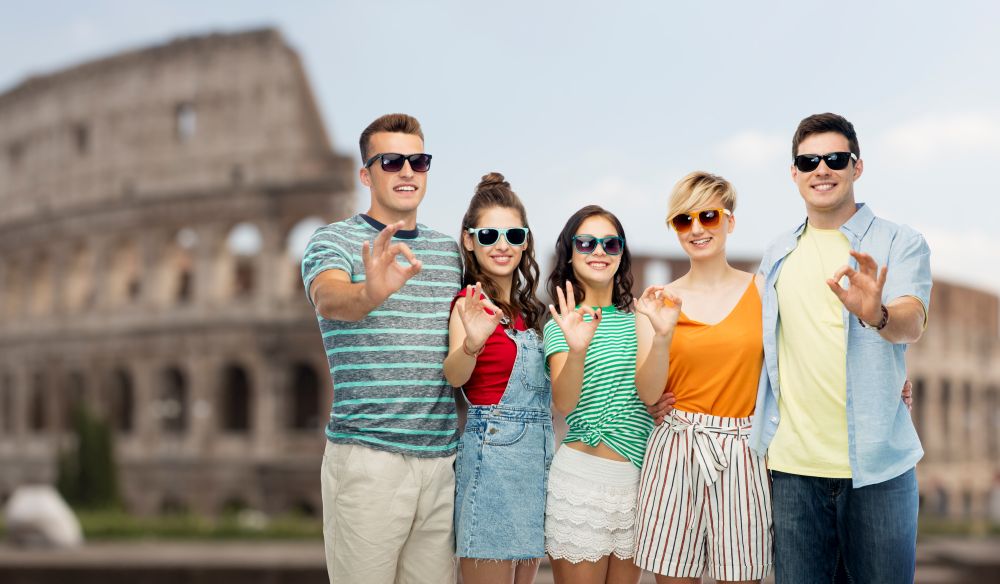 travel, tourism and summer holidays concept - group of happy smiling friends in sunglasses showing ok hand sign over coliseum background. friends in sunglasses showing ok over coliseum