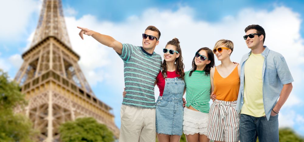 travel, tourism and summer holidays concept - group of happy smiling friends in sunglasses pointing finger to something over eiffel tower background. friends in sunglasses over eiffel tower background
