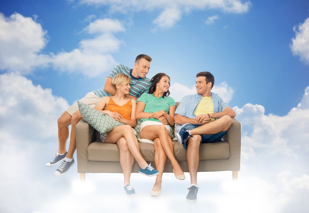 friendship, leisure and people concept - group of happy smiling friends sitting on sofa over blue sky and clouds background. friends sitting on sofa over background