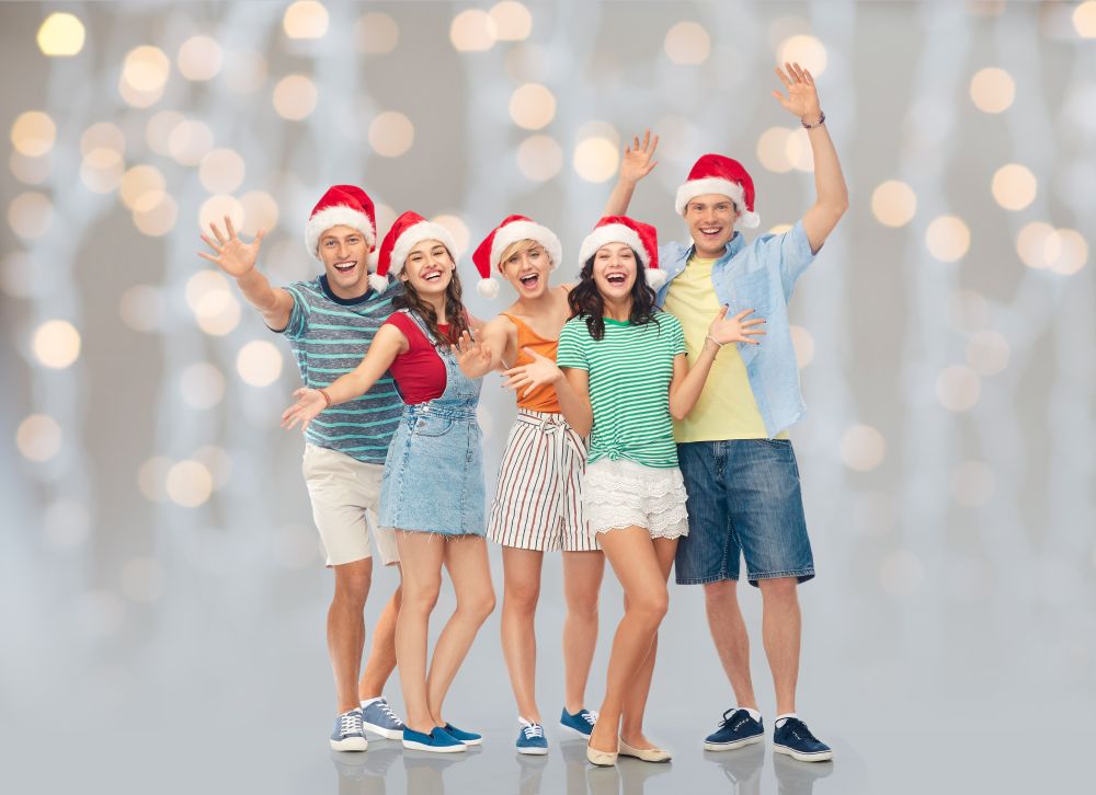 christmas, holidays and friendship concept - group of happy smiling friends in santa hats having fun over festive lights background. happy friends in santa hats over festive lights
