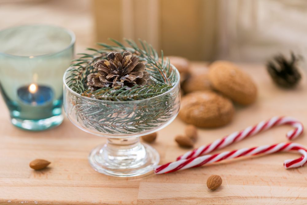 christmas concept - decoration of fir twig with pinecone in ice cream glass or dessert bowl, candy canes and cookies. christmas fir decoration with cone in dessert bowl