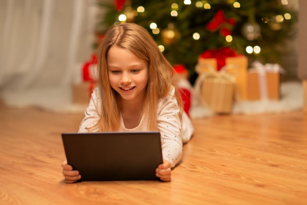 christmas, holidays and childhood concept - smiling girl with tablet pc computer at home. smiling girl with tablet pc at christmas home