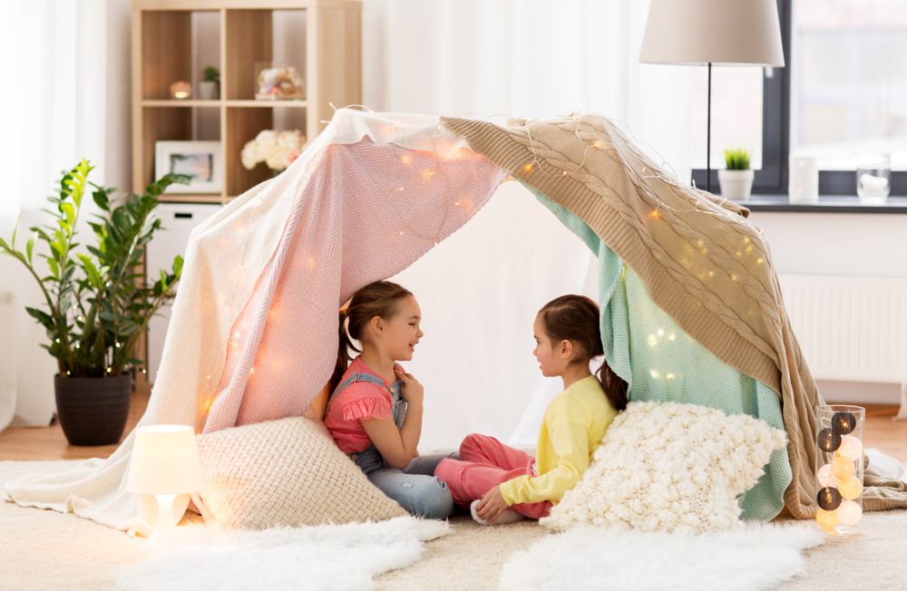 childhood, hygge and friendship concept - little girls talking in kids tent or teepee at home. little girls talking in kids tent at home