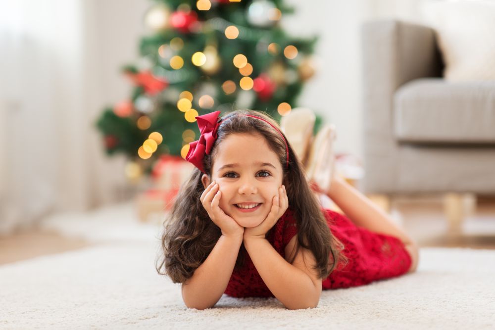 christmas, holidays and childhood concept - happy little girl lying on floor at home. happy girl lying on floor at home on christmas
