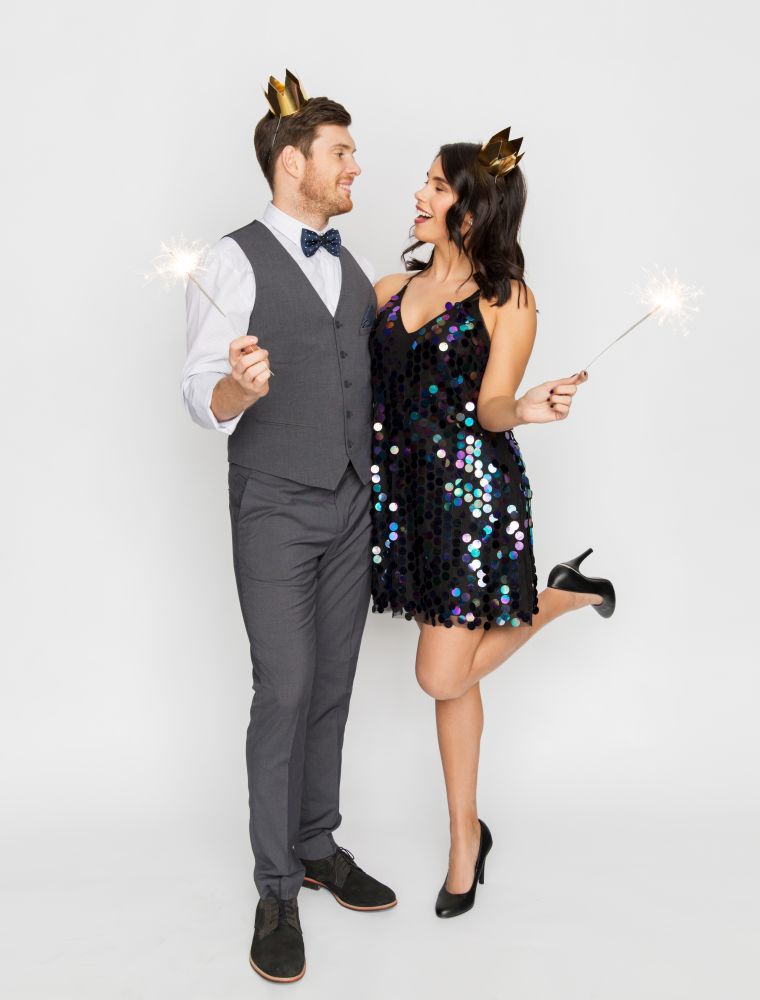 celebration, fun and holidays concept - happy couple with crowns and sparklers at party. happy couple with crowns and sparklers at party