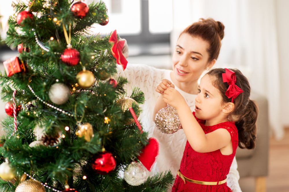 family, winter holidays and people concept - happy mother and little daughter decorating christmas tree at home. happy family decorating christmas tree at home