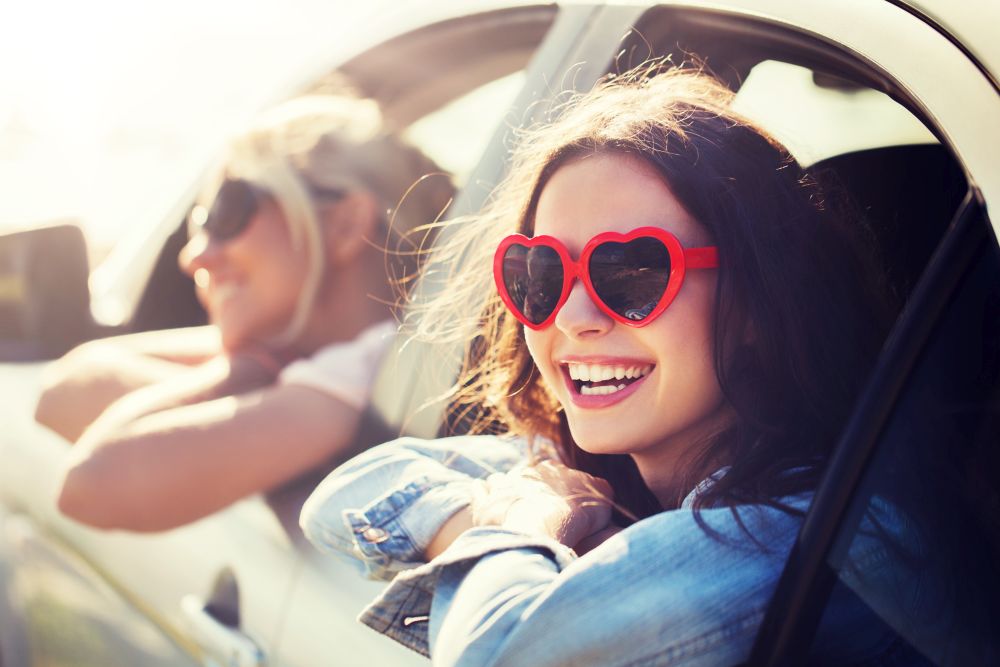 summer holidays, valentines day, travel, road trip and people concept - happy teenage girls or young women heart shaped sunglasses in car at seaside. happy teenage girls or women in car at seaside