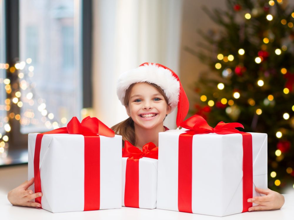 holidays and childhood concept - happy girl with gift boxes at home over room with christmas tree background. happy girl with christmas gifts at home