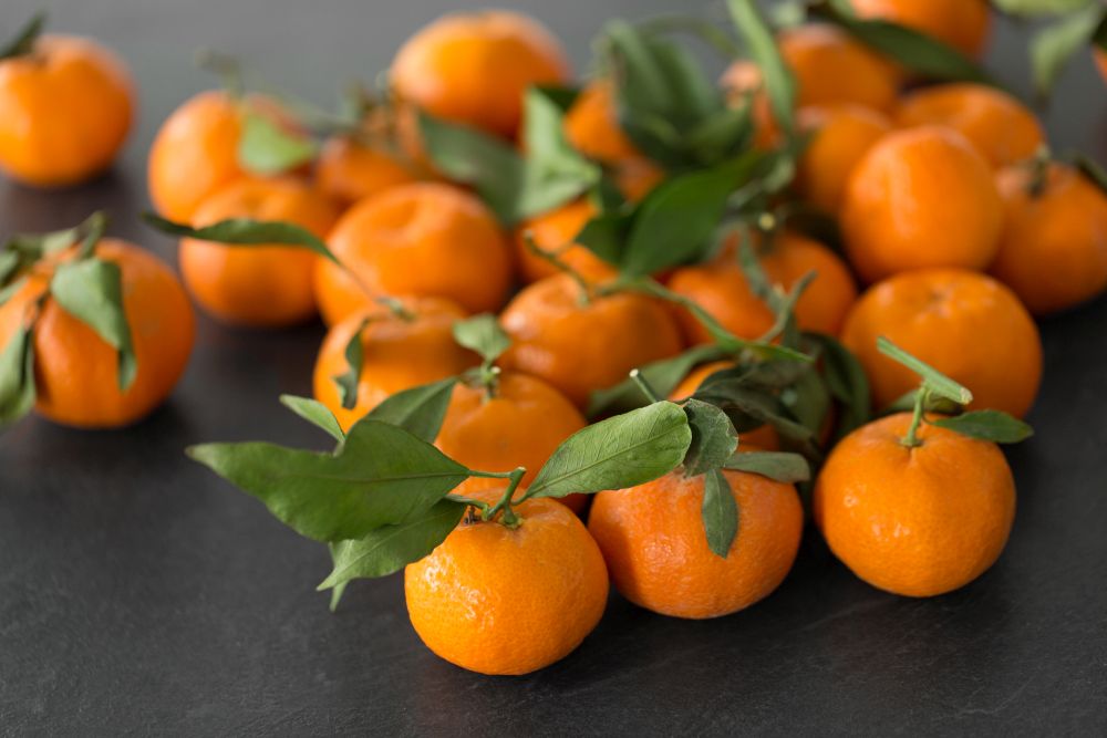 food, healthy eating and vegetarian concept - close up of whole mandarins with leaves on slate table top. close up of mandarins on slate table top